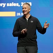 Man standing and smiling on stage in front of graph on large projection